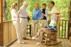 A multi-generational family talks together on a wooden porch, the grandmother in a rocking chair